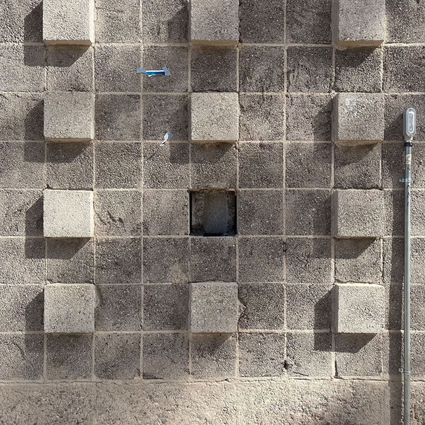 photo of a semi-decorative masonry wall with square units, some projecting, one missing